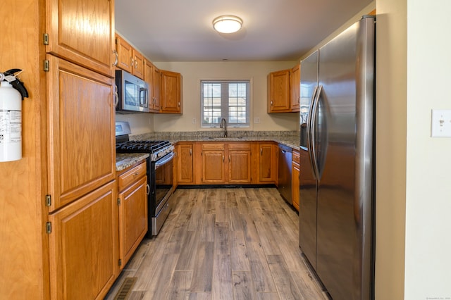 kitchen with appliances with stainless steel finishes, light stone countertops, sink, and wood-type flooring