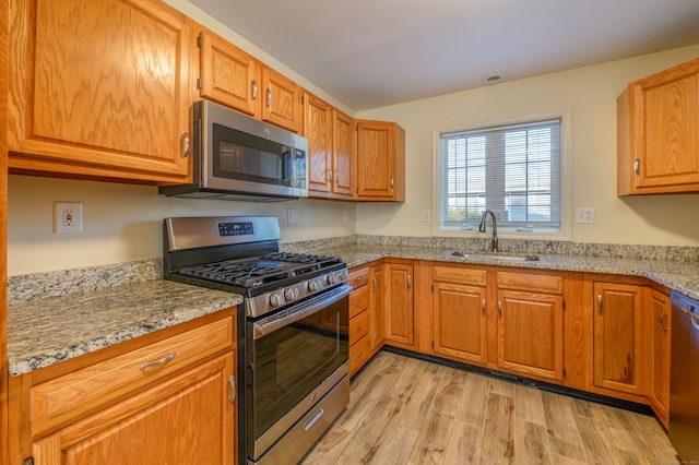 kitchen with light stone counters, sink, stainless steel appliances, and light hardwood / wood-style floors