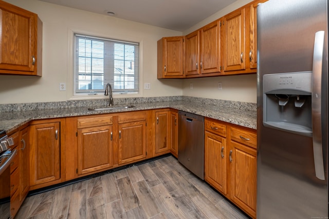 kitchen with stainless steel appliances, hardwood / wood-style flooring, light stone countertops, and sink