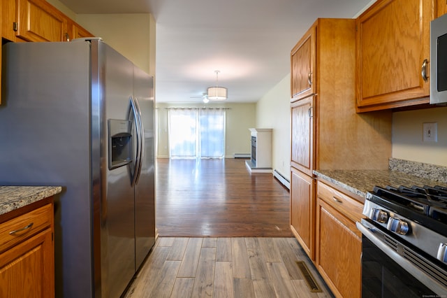 kitchen featuring light hardwood / wood-style flooring, baseboard heating, hanging light fixtures, stainless steel appliances, and light stone countertops