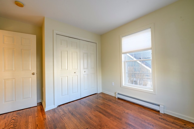 unfurnished bedroom featuring a baseboard radiator, dark hardwood / wood-style floors, and a closet