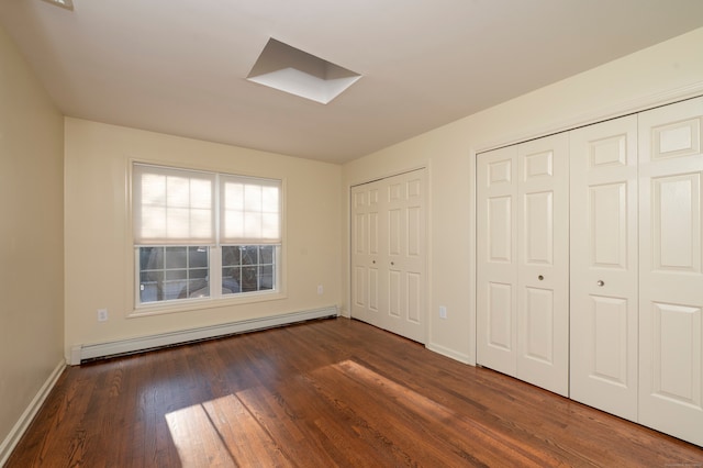 unfurnished bedroom with a baseboard radiator, dark hardwood / wood-style flooring, a skylight, and two closets