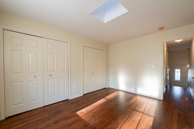 unfurnished bedroom with multiple closets, dark hardwood / wood-style flooring, and a skylight