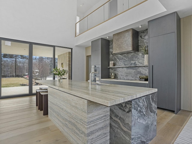 kitchen featuring wall chimney range hood, modern cabinets, light wood-style floors, and gray cabinetry