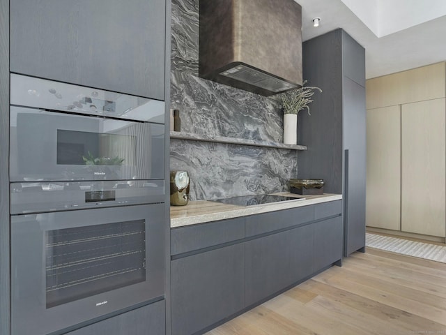 kitchen with gray cabinets, decorative backsplash, double oven, wall chimney range hood, and black electric cooktop