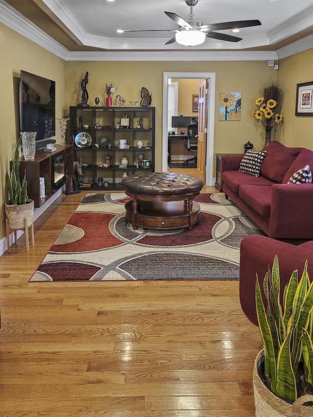 living room with crown molding, ceiling fan, wood-type flooring, and a raised ceiling