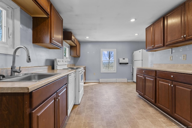 kitchen with baseboards, light countertops, recessed lighting, white appliances, and a sink