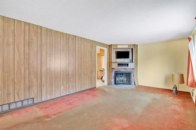 unfurnished living room featuring a fireplace, carpet floors, wooden walls, and a textured ceiling