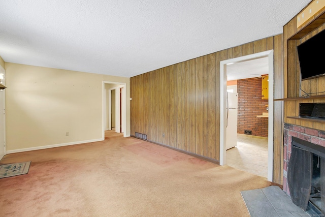 unfurnished living room featuring a brick fireplace, light carpet, wood walls, and a textured ceiling