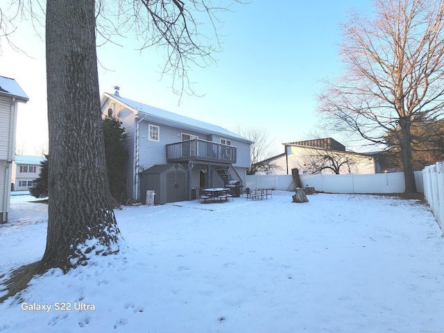 snow covered property with a wooden deck and a storage unit