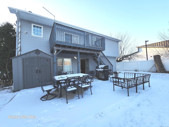 snow covered back of property featuring a storage unit and a deck