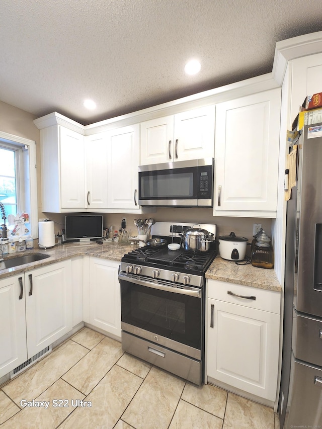 kitchen featuring stainless steel appliances, white cabinetry, and a textured ceiling