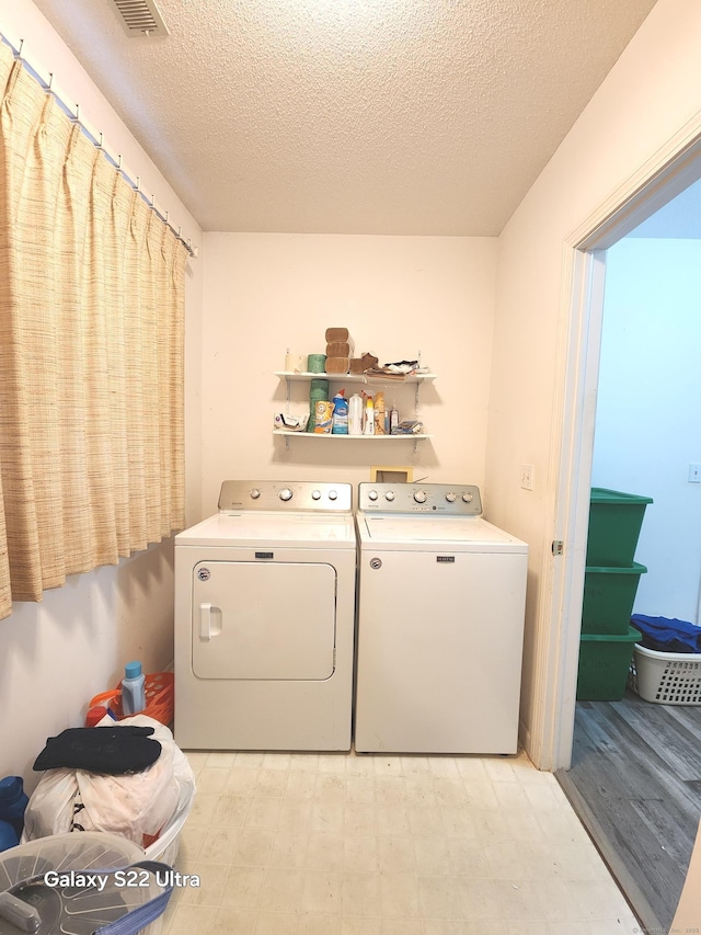 laundry room featuring light hardwood / wood-style flooring, washer and dryer, and a textured ceiling