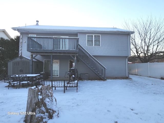 snow covered back of property featuring a deck and a storage unit