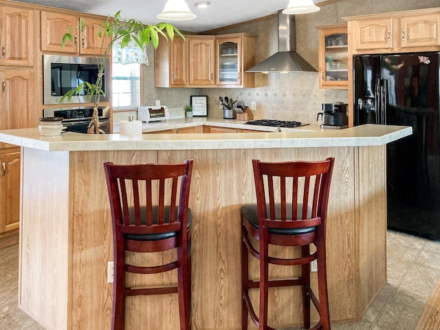 kitchen featuring wall chimney range hood, stainless steel appliances, a kitchen breakfast bar, and a spacious island