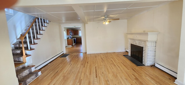 unfurnished living room featuring baseboard heating, ceiling fan, a fireplace, and light hardwood / wood-style flooring