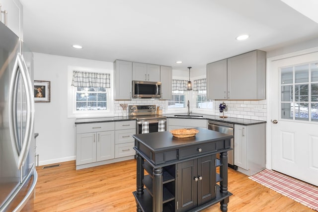 kitchen featuring open shelves, a sink, appliances with stainless steel finishes, dark countertops, and light wood-type flooring