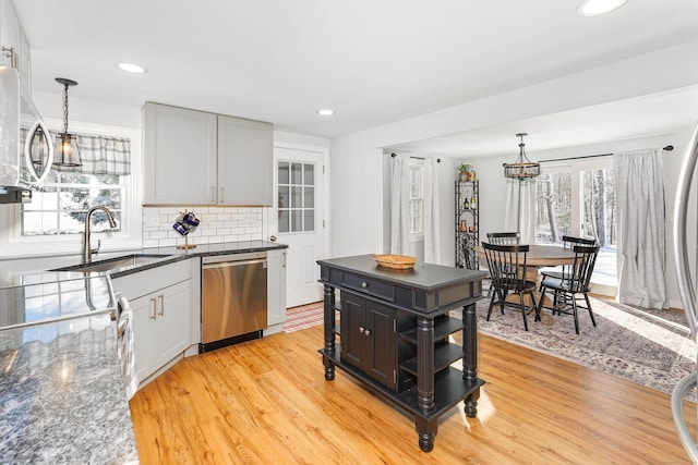 kitchen featuring backsplash, dishwasher, pendant lighting, light wood-type flooring, and dark stone counters