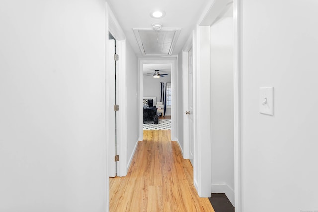 corridor with attic access, light wood-type flooring, and baseboards