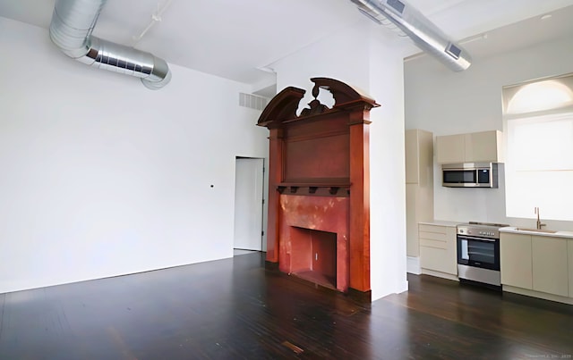 kitchen featuring sink, a towering ceiling, stainless steel appliances, dark hardwood / wood-style flooring, and cream cabinetry