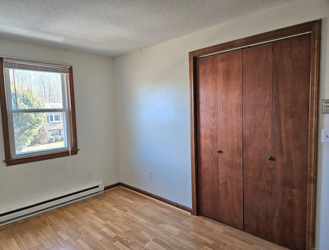 unfurnished bedroom featuring a baseboard heating unit, light hardwood / wood-style floors, a closet, and a textured ceiling