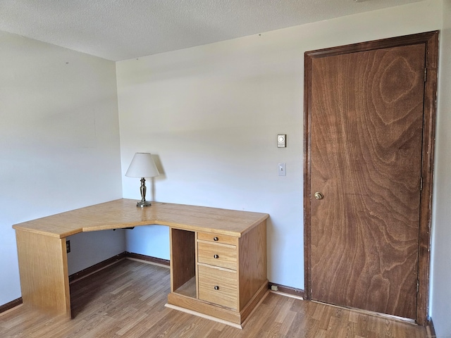 unfurnished office featuring wood-type flooring, built in desk, and a textured ceiling