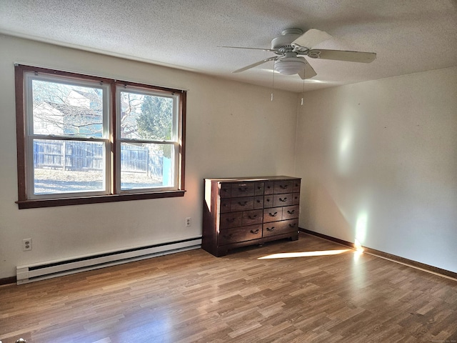 unfurnished bedroom featuring ceiling fan, a baseboard heating unit, a textured ceiling, and light wood-type flooring