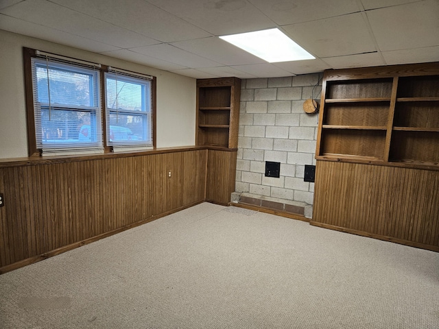 basement featuring light carpet, wooden walls, built in features, and a paneled ceiling