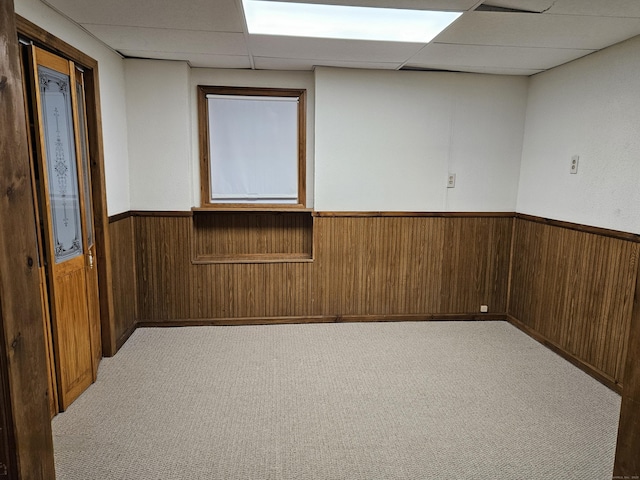 carpeted spare room with a drop ceiling and wood walls