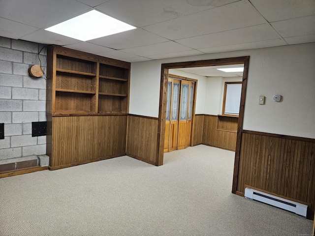 empty room featuring light carpet, a baseboard heating unit, wooden walls, and a paneled ceiling