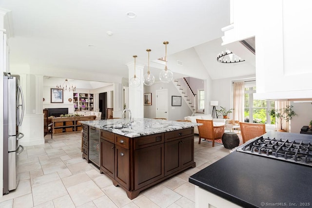 kitchen with sink, appliances with stainless steel finishes, dark brown cabinets, light stone counters, and vaulted ceiling