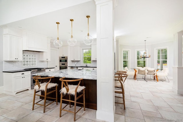 kitchen featuring dark stone countertops, appliances with stainless steel finishes, a kitchen breakfast bar, an island with sink, and white cabinets