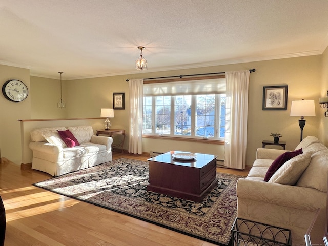 living room with wood-type flooring, ornamental molding, a notable chandelier, baseboard heating, and a textured ceiling