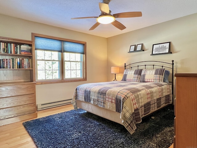 bedroom featuring ceiling fan, wood-type flooring, a textured ceiling, and a baseboard heating unit