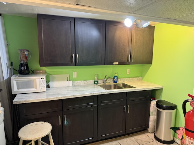 kitchen featuring a paneled ceiling, sink, dark brown cabinets, and light tile patterned floors