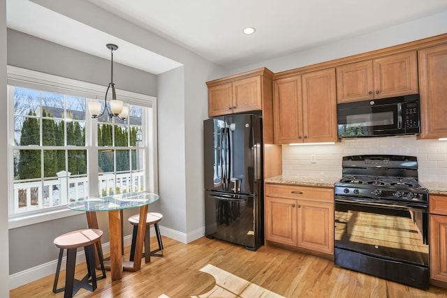 kitchen featuring light stone counters, backsplash, light hardwood / wood-style flooring, and black appliances