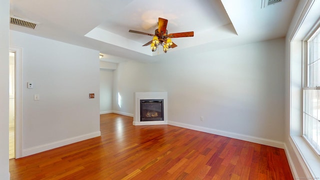 unfurnished living room featuring a raised ceiling, wood-type flooring, and ceiling fan