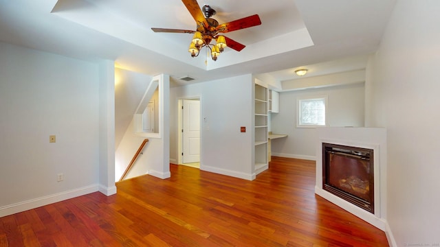 unfurnished living room with wood-type flooring, ceiling fan, and a tray ceiling