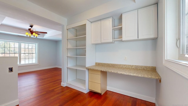 unfurnished office featuring ceiling fan, a tray ceiling, dark hardwood / wood-style flooring, and built in desk