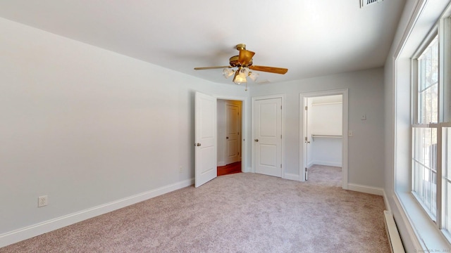 unfurnished bedroom featuring a spacious closet, ceiling fan, baseboard heating, light carpet, and a closet