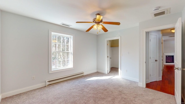 unfurnished bedroom with carpet, a baseboard heating unit, a spacious closet, ceiling fan, and a closet