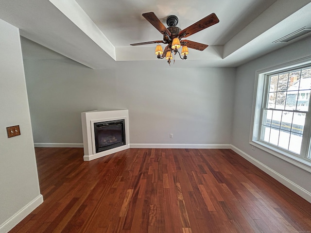 unfurnished living room with a tray ceiling, dark hardwood / wood-style floors, and ceiling fan