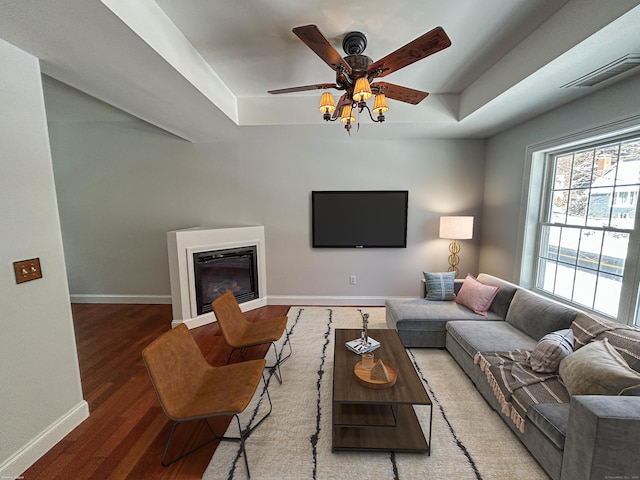 living room featuring a raised ceiling, hardwood / wood-style flooring, and ceiling fan