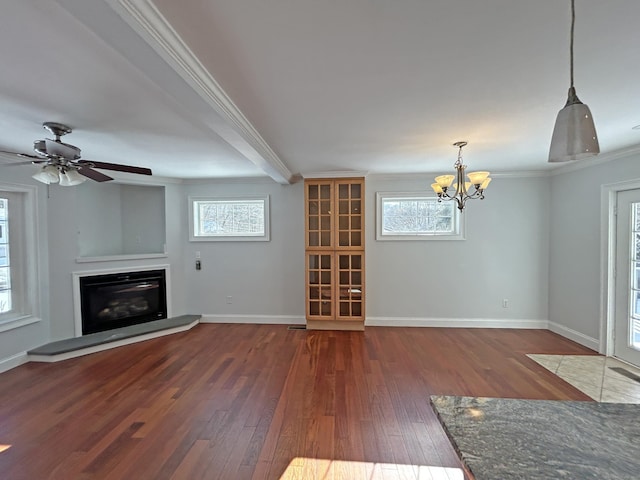 unfurnished living room featuring ornamental molding, ceiling fan with notable chandelier, dark wood-type flooring, and a wealth of natural light