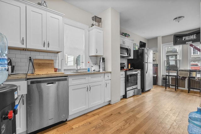 kitchen with sink, white cabinetry, stainless steel appliances, light hardwood / wood-style floors, and decorative backsplash