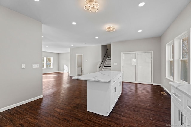 kitchen with white cabinetry, dark hardwood / wood-style flooring, light stone countertops, and a kitchen island