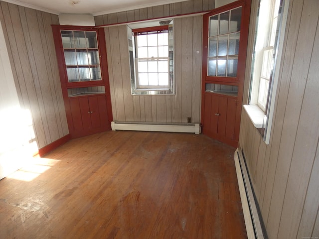 unfurnished dining area with a baseboard heating unit, crown molding, dark wood-type flooring, and wooden walls