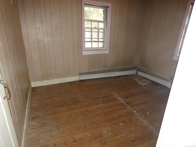 empty room featuring wood walls, dark hardwood / wood-style floors, and baseboard heating