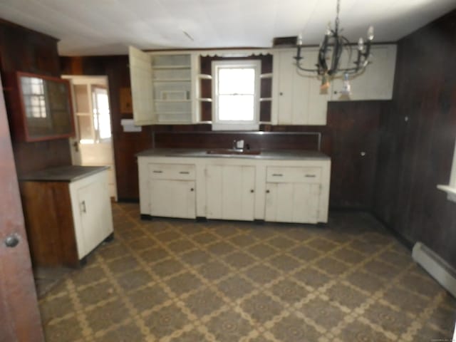 kitchen with wooden walls, sink, white cabinets, hanging light fixtures, and baseboard heating