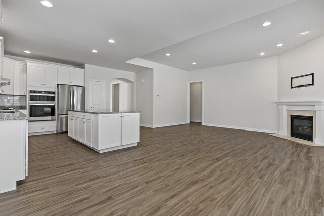 kitchen with white cabinetry, a kitchen island with sink, stainless steel appliances, light stone counters, and dark hardwood / wood-style flooring